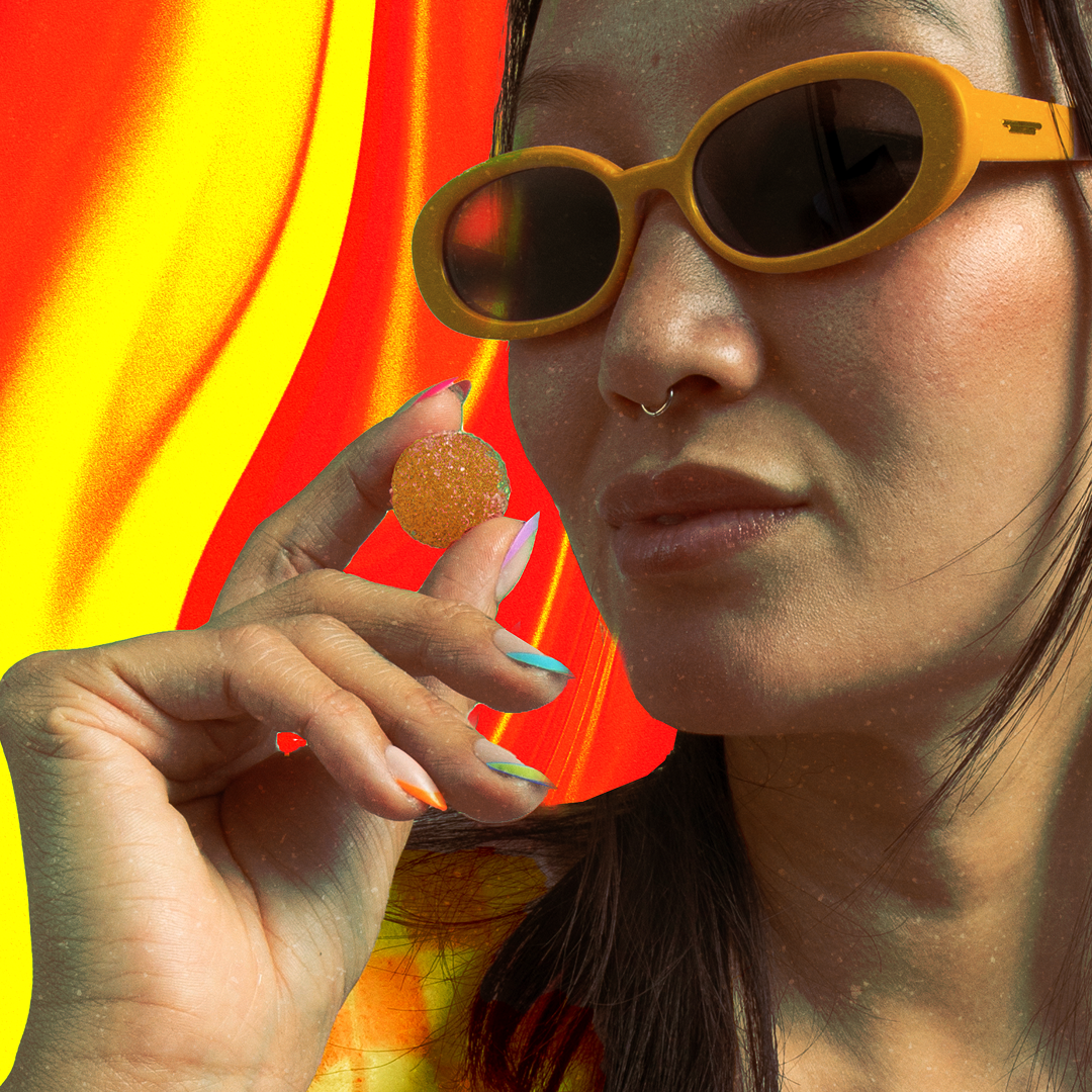Person wearing yellow sunglasses holding a sugar-coated lemon gummy between thumb and forefinger, colorful nails visible